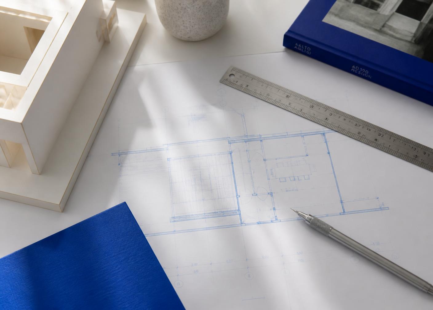 An architect's drafting table with a blue technical drawing, ruler and pencil